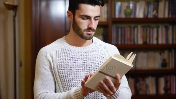 Knappe jongeman die thuis een boek leest in zijn woonkamer — Stockvideo