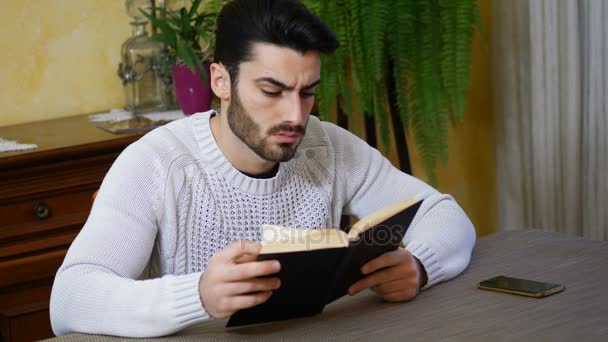 Jovem homem lendo livro em casa em sua sala de estar — Vídeo de Stock