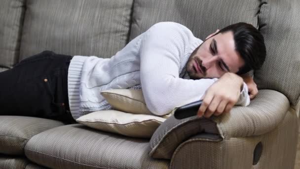 Joven hombre aburrido sentado en el sofá viendo la televisión — Vídeos de Stock