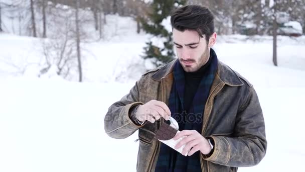 Handsome young man biting chocolate in snow — Stock Video