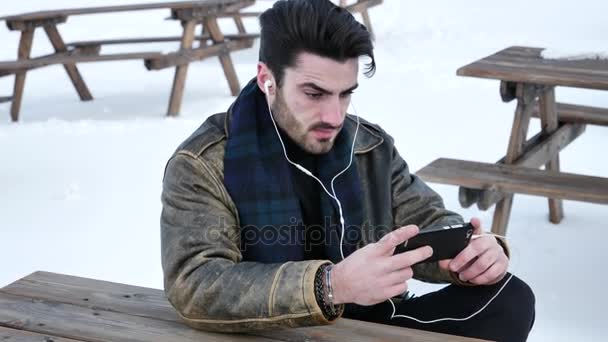 Молодой человек со смартфоном в снегу — стоковое видео