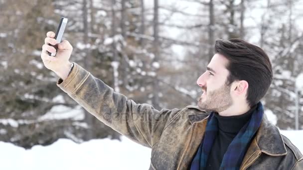Молодой человек делает селфи в снегу — стоковое видео