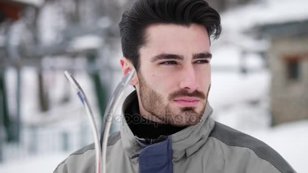 Красивий чоловік з лижами, що стоїть у снігу — стокове відео
