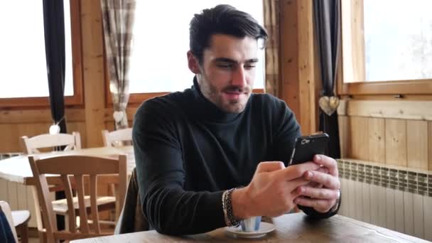 Hombre guapo usando el teléfono celular en la acogedora estación de esquí — Vídeo de stock