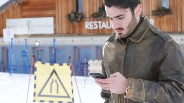 Jeune homme avec smartphone dans la neige — Video