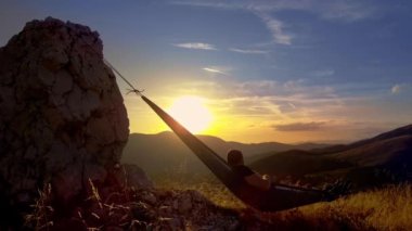 man relaxing in hammock at sunset in the mountains