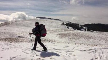 Sırt çantalı, dağ sırtında yürüyen, derin karla kaplı bir fotoğrafçı.