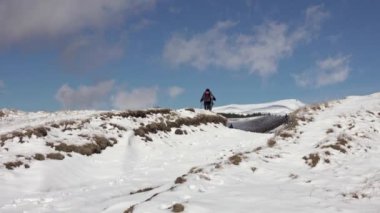 Sırt çantalı, dağ sırtında yürüyen, derin karla kaplı bir fotoğrafçı.