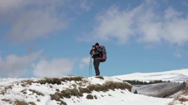 Sırt çantalı, dağ sırtında yürüyen, derin karla kaplı bir fotoğrafçı.