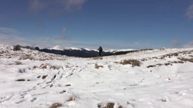 Sırt çantalı, dağ sırtında yürüyen, derin karla kaplı bir fotoğrafçı.