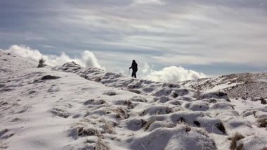 Sırt çantasıyla dağ sırtında yürüyen, derin karla kaplı bir yürüyüşçü.