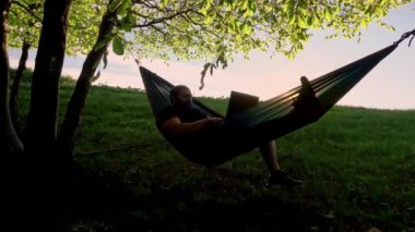 man working outdoors with laptop in hammock