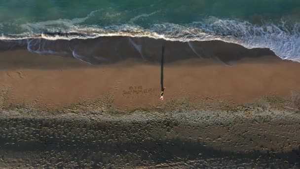 在日落前的黄金时刻 一架无人驾驶飞机飞越了一个金发碧眼的女人 她在美丽的沙滩上写下了 的字样 沙滩上还有碧绿的大海 — 图库视频影像
