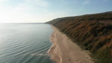 Etrafı turkuaz yeşil deniz ve sabah aşırı gelişmiş dağ yamaçlarıyla çevrili güzel, uçsuz bucaksız kumlu sahil üzerinde İHA uçuşu.