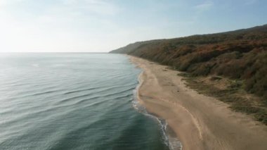 Etrafı turkuaz yeşil deniz ve sabah aşırı gelişmiş dağ yamaçlarıyla çevrili güzel, uçsuz bucaksız kumlu sahil üzerinde İHA uçuşu.