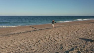Uzun sarı saçlı genç bir kadınla video, gün batımından önce güzel tropikal kumsalda dönüyor ve yürüyor.