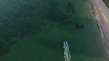 Güneş batmadan önce açık yeşil deniz suyuyla sürat teknesinin üzerinde uçan hava aracı