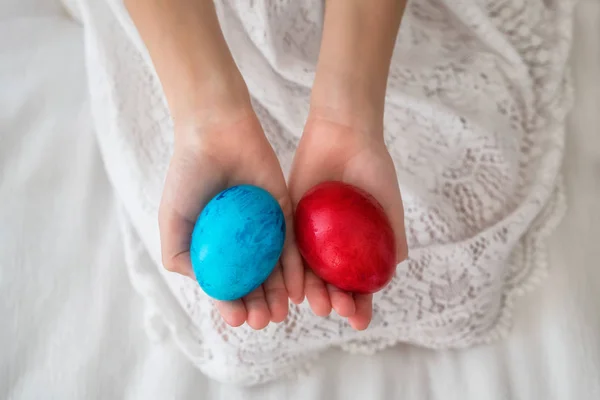 复活节的概念 用小女孩的手握住画在红色和蓝色复活节彩蛋上的近景 — 图库照片