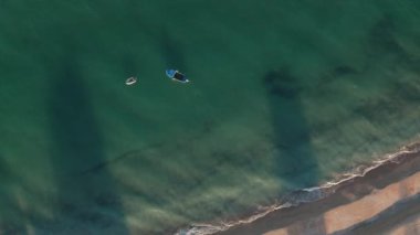 Güzel, uçsuz bucaksız kumlu sahil ve turkuaz yeşil denizdeki tekneler üzerinde rotasyonlu İHA uçuşu.
