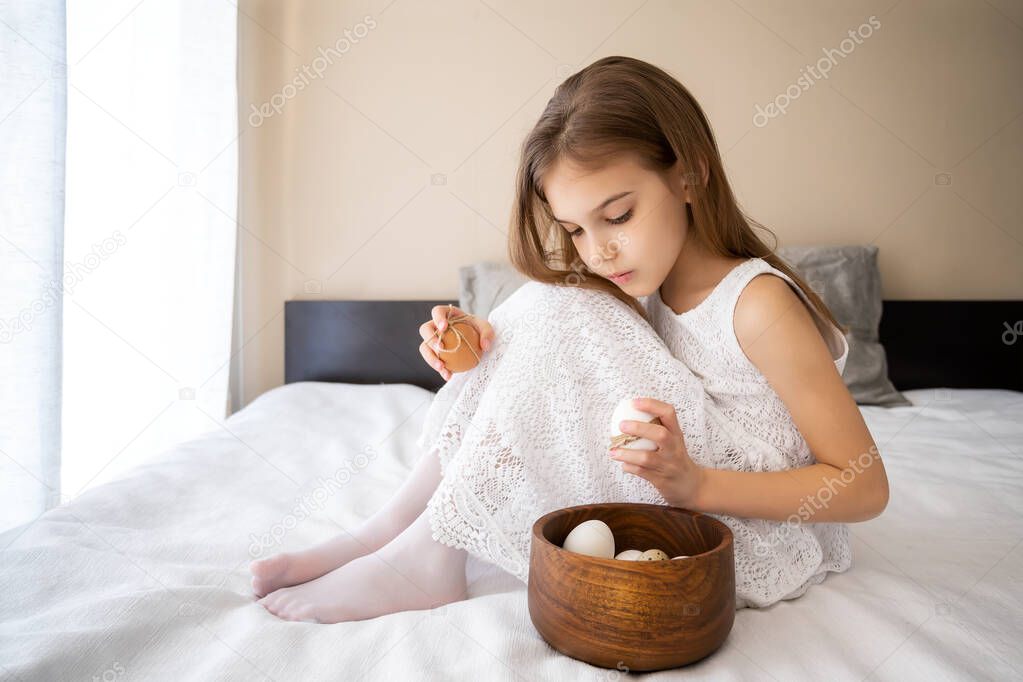 Little girl in white dress playing with white and beige unpainted eggs 