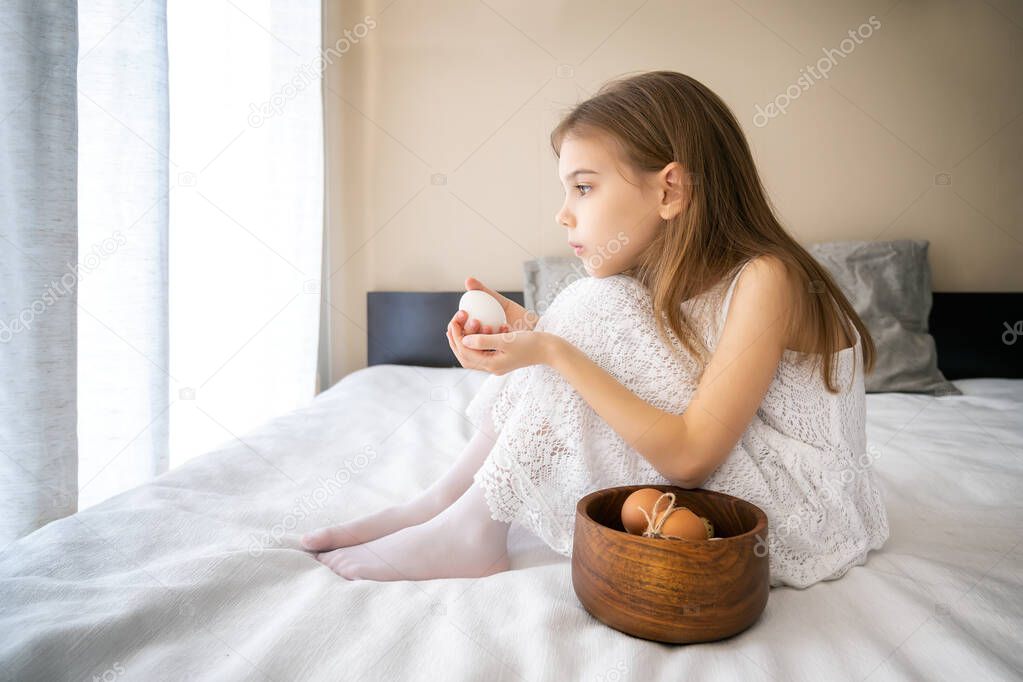Little girl in white dress playing with white and beige unpainted eggs 