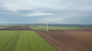 Bahar tarlaları boyunca rüzgar türbinlerinin etrafında uçan hava. Temiz ve Yenilenebilir Rüzgâr Güç Çiftliği hareket halinde. Yeşil enerji, sürdürülebilir alternatif elektrik, kirlilik ortamı yok.