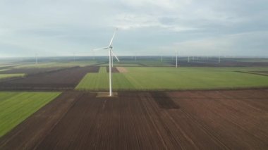 Bahar tarlaları boyunca rüzgar türbinlerinin etrafında uçan hava. Temiz ve Yenilenebilir Rüzgâr Güç Çiftliği hareket halinde. Yeşil enerji, sürdürülebilir alternatif elektrik, kirlilik ortamı yok.