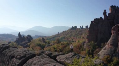 Beyaz gömlekli, özgürlüğünü hisseden genç bir sarışının etrafında uçuşan hava, sonbahar ormanı Belogradchik Kayalıkları, Bulgaristan 'daki çarpıcı kaya oluşumunun kenarında duruyor..