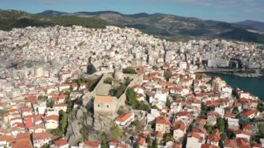 Yunanistan 'ın kuzeyindeki Kavala şehrinin üzerinde insansız hava aracı uçuşu, eski kasaba, kırmızı çatıları ve ortaçağ şehir duvarı olan evler, tekneleri olan yeni kasaba ve marina.
