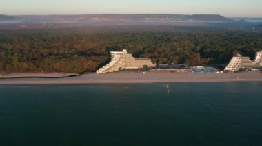 Sabahın erken saatlerinde turkuaz yeşil deniz ve kıyı otelleriyle dolu güzel kumlu sahil üzerindeki İHA uçuşu, Bulgaristan 'ın Albena tatil beldesindeki Karadeniz kıyısı