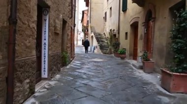 İTALYA, PIENZA - 11 Nisan 2019: Eski Toskana köyü Pienza 'nın dar sokaklarında, eski taş duvarlarla, çiçeklerle kaplanmış cepheleriyle sabah erken saatlerde düzgün bir kamera kaydı