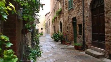 İTALYA, PIENZA - 11 Nisan 2019: Eski Toskana köyü Pienza 'nın dar sokaklarında, eski taş duvarlarla, çiçeklerle kaplanmış cepheleriyle sabah erken saatlerde düzgün bir kamera kaydı