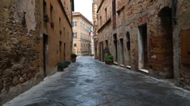İTALYA, PIENZA - 11 Nisan 2019: Eski Toskana köyü Pienza 'nın dar sokaklarında, eski taş duvarlarla, çiçeklerle kaplanmış cepheleriyle sabah erken saatlerde düzgün bir kamera kaydı