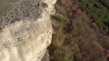 Sonbahar ormanı ve mavi gökyüzü ile çevrili çarpıcı kaya oluşumunun kenarında yürüyen genç sarışın bir kadının dikiz aynasıyla uçan.