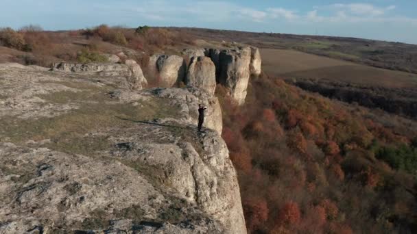Vol aérien autour d'une jeune femme prenant des photos sur son téléphone intelligent tout en se tenant au bord de la formation rocheuse étonnante entourée par la forêt d'automne 