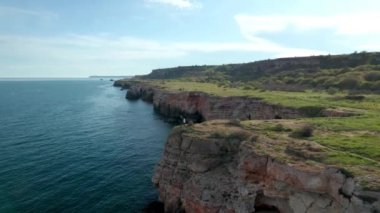 Anne ve kızının yeşil tarlaları ve ağaçları olan kayalık bir sahil şeridinin kenarında durduğu panoramik bir video. Karadeniz kıyısında bahar zamanı, Yailata - Bulgaristan 'ın ulusal arkeoloji ve doğa rezervi.