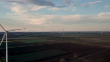 Bahar tarlaları boyunca rüzgar türbinlerinin etrafında uçan hava. Temiz ve Yenilenebilir Rüzgâr Güç Çiftliği hareket halinde. Yeşil enerji, sürdürülebilir alternatif elektrik, kirlilik ortamı yok. Görüntüyü kapat.