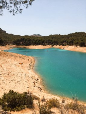 İnsanlar yazın gölün tadını çıkarırken ağaçların tepesinden göle doğru yükselen manzara. Ardales, Malaga.