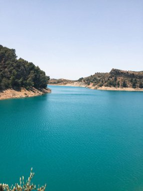 İnsanlar yazın gölün tadını çıkarırken ağaçların tepesinden göle doğru yükselen manzara. Ardales, Malaga.