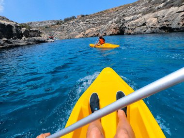 Turistler Malta 'nın Gozo adasındaki plajlardan birinde kano çalışması yapıyorlar. İnsanlar sahilde yazın tadını çıkarıyor..