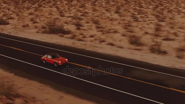に沿って赤いクラシック車が上のヘッドライトが夕暮れ時に砂漠の道を荒涼とした空撮 — ストック動画