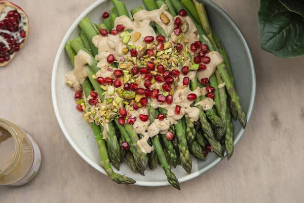 Tahini soslu kuşkonmaz, şam fıstığı ve nar. Tabak ellerde, üst görünüm.