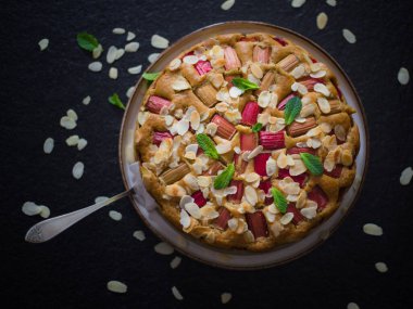 Bir fırın. Hazır, taze ev yapımı raventli kek ve nane yapraklarıyla süslenmiş badem gevreği. Kırsal tarzda. Taştan siyah bir masada. Üst görünüm.