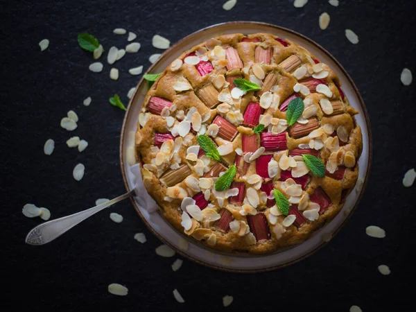 Bir fırın. Hazır, taze ev yapımı raventli kek ve nane yapraklarıyla süslenmiş badem gevreği. Kırsal tarzda. Taştan siyah bir masada. Üst görünüm.