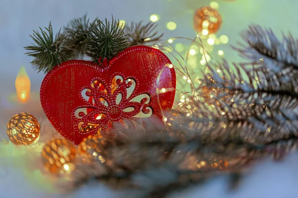 Jouet de Noël coeur rouge avec ornement sur la neige. Guirlande et branches de pin sur cristaux de glace. Fond flou et bokeh . — Photo