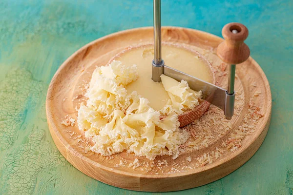 Fromage français Monk Head tranché sur une surface ronde en bois. Couteau pour trancher et déguster de savoureuses chips de fromage sur une table verte . Photo De Stock