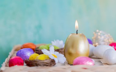 Paskalya kartı yanan altın mum ve renkli folyoyla çikolatalı yumurta. Geçmişi ve ışıldayan bokeh. Boşluğu kopyala.