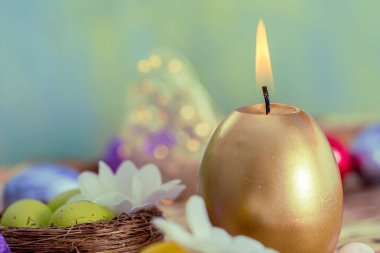 Paskalya kartı yanan altın mum ve renkli folyoda sarı yumurtalar. Geçmişi ve ışıldayan bokeh. Boşluğu kopyala.