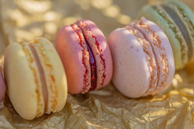 Altın kağıt üzerinde makarna, güneş ışığı ve gölgeler. Lezzetli, tatlı, havadar, renkli Fransız pastaları.. 