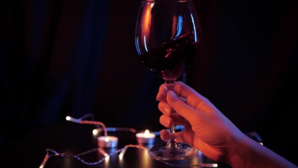 Vista en cámara lenta de cerca de ondear vino tinto en una copa por las mujeres entregan fondo oscuro con dos velas y guirnaldas de Navidad. Control de calidad del vino tinto — Vídeo de stock